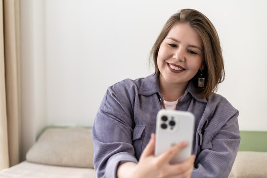 Plus size smiling young woman taking selfie with mobile phone.