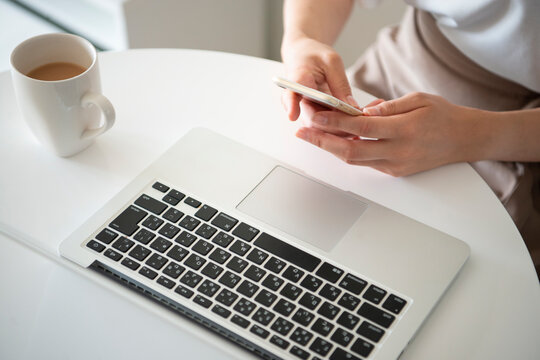 パソコンの前でスマホを触っている女性の手元