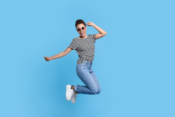 Fototapeta na wymiar Happy young woman jumping while dancing on light blue background