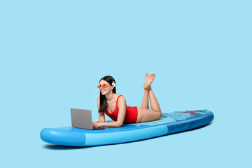 Obraz premium Happy woman with laptop on SUP board against light blue background