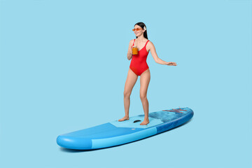 Happy woman with refreshing drink on SUP board against light blue background