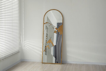 Broken mirror with many cracks near white wall indoors