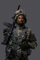 Dark skinned soldier in NATO uniform and helmet poses with a serious expression on a plain grey background