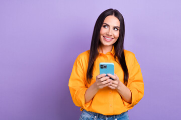 Portrait of interested woman with long hairstyle wear oversize shirt hols phone look empty space offer isolated on violet color background