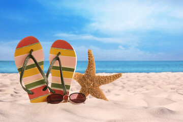 Fototapeta na wymiar Flip flops with sunglasses and starfish on sunny ocean beach, space for text. Summer vacation