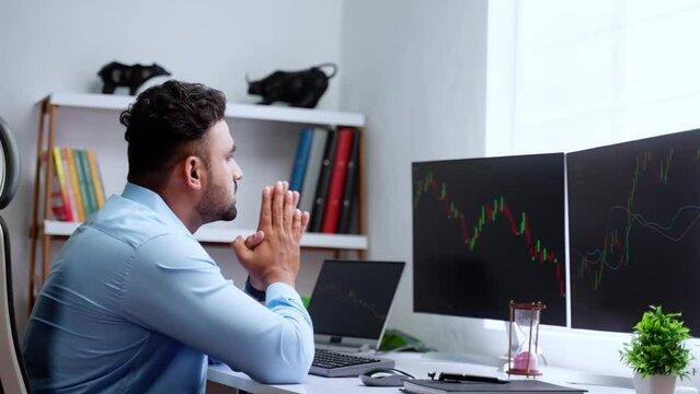 Worried indian trader praying to god to make profit from stock market while trading in front of monitor - concept of Investor faith, Market fluctuations and anxiety