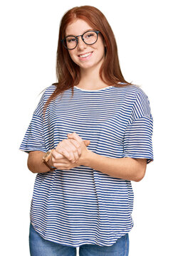 Young read head woman wearing casual clothes and glasses with hands together and crossed fingers smiling relaxed and cheerful. success and optimistic
