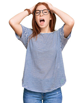 Young read head woman wearing casual clothes and glasses crazy and scared with hands on head, afraid and surprised of shock with open mouth
