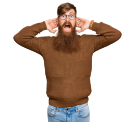 Young irish redhead man wearing casual clothes and glasses crazy and scared with hands on head, afraid and surprised of shock with open mouth