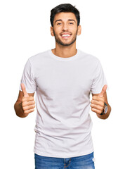 Young handsome man wearing casual white tshirt success sign doing positive gesture with hand, thumbs up smiling and happy. cheerful expression and winner gesture.