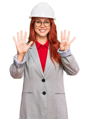 Young redhead woman wearing architect hardhat showing and pointing up with fingers number nine while smiling confident and happy.