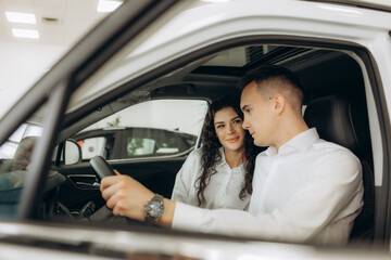 Happy millennial couple taking car key from auto salesman, sitting inside modern automobile at dealership, panorama. Cheery young family buying new vehicle at modern showroom.