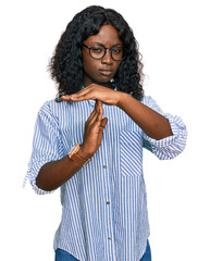 Beautiful african young woman wearing casual clothes and glasses doing time out gesture with hands,...