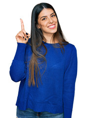 Young hispanic woman wearing casual clothes showing and pointing up with finger number one while...