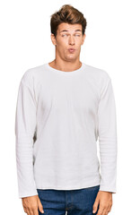 Handsome caucasian man wearing casual white sweater making fish face with lips, crazy and comical gesture. funny expression.