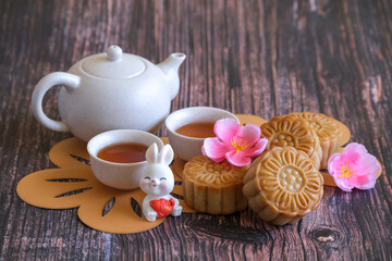 Chinese Mid-Autumn Festival concept made from mooncakes, tea decorated with plum blossom and rabbits on wooden background.