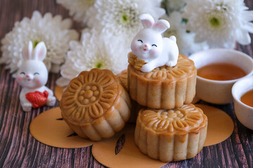 Chinese Mid-Autumn Festival concept made from mooncakes, tea decorated with Chrysanthemum blossom and rabbit on wooden background.