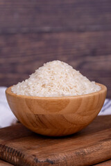 Rice on wood background. Uncooked dry rice in wooden bowl. Close up