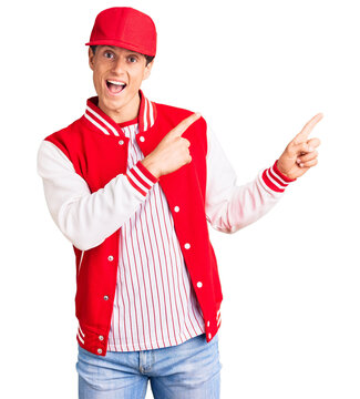 Young handsome man wearing baseball uniform smiling and looking at the camera pointing with two hands and fingers to the side.
