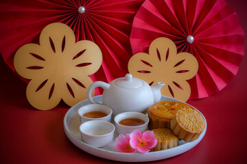 Chinese Mid-Autumn Festival concept made from mooncakes, tea decorated with plum blossom, rabbit and red paper fans on red background.