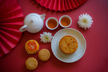 Chinese Mid-Autumn Festival concept made from mooncakes, tea decorated with Chrysanthemum blossom, rabbit and red paper fans on red background.