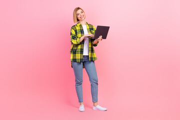 Full length photo of attractive young woman hold device laptop dressed stylish checkered yellow outfit isolated on pink color background