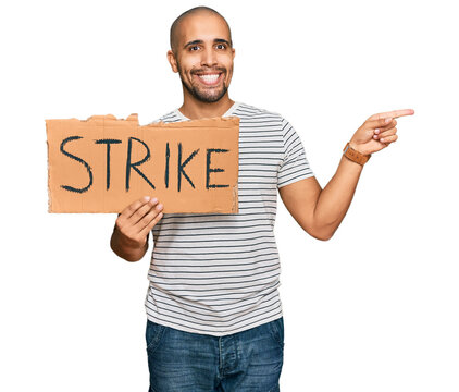 Hispanic adult man holding strike banner cardboard smiling happy pointing with hand and finger to the side
