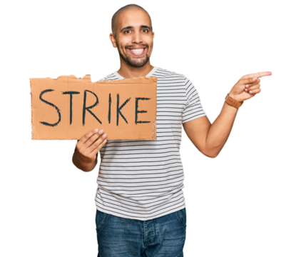 Hispanic adult man holding strike banner cardboard smiling happy pointing with hand and finger to the side