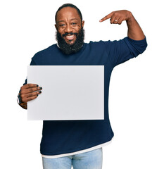 Young african american man holding blank empty banner pointing finger to one self smiling happy and...