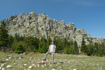 The guy, a tourist, stands tall against the background of a rock. Summer, day, blue sky.