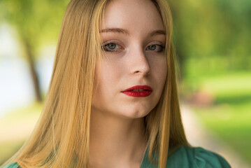 Naklejka premium Portrait of a girl in a green dress on a walk on a sunny summer day in the park.