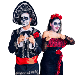 Young couple wearing mexican day of the dead costume over background pointing fingers to camera with happy and funny face. good energy and vibes.