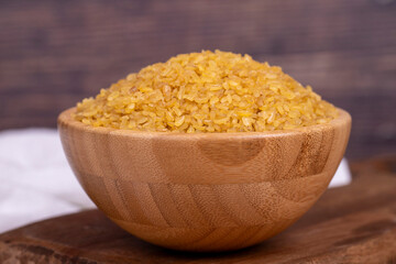 Bulgur on wood background. Bulgur wheat grains in wooden bowl. Close up