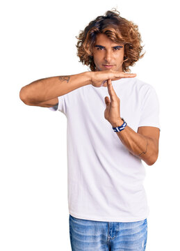 Young hispanic man wearing casual white tshirt doing time out gesture with hands, frustrated and serious face