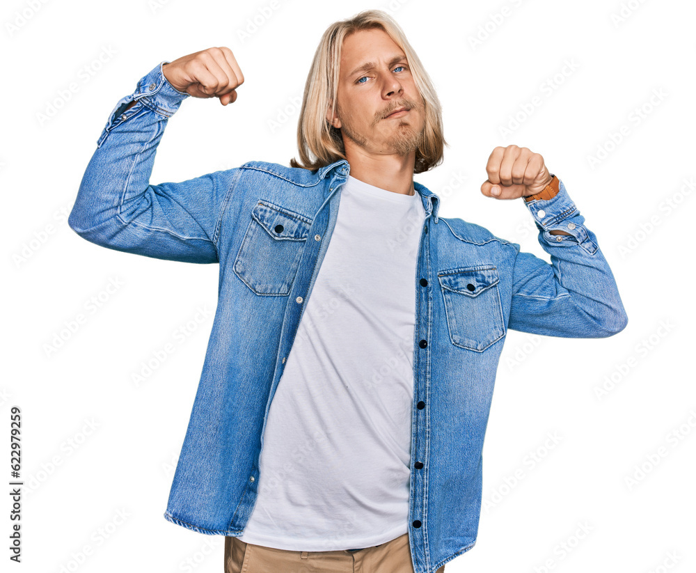 Wall mural Caucasian man with blond long hair wearing casual denim jacket showing arms muscles smiling proud. fitness concept.