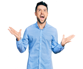 Hispanic man with beard wearing casual business shirt crazy and mad shouting and yelling with aggressive expression and arms raised. frustration concept.