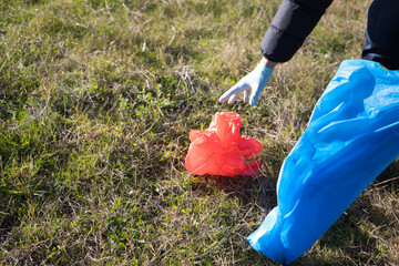 Detail of a volunteer's hand picking up a red plastic bag from the forest. Concept of Earth Day and...