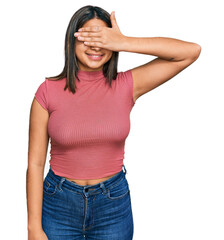 Young hispanic girl wearing casual t shirt smiling and laughing with hand on face covering eyes for surprise. blind concept.