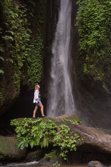 Travel lifestyle. Young traveler woman at waterfall in tropical forest. Leke Leke waterfall, Bali, Indonesia