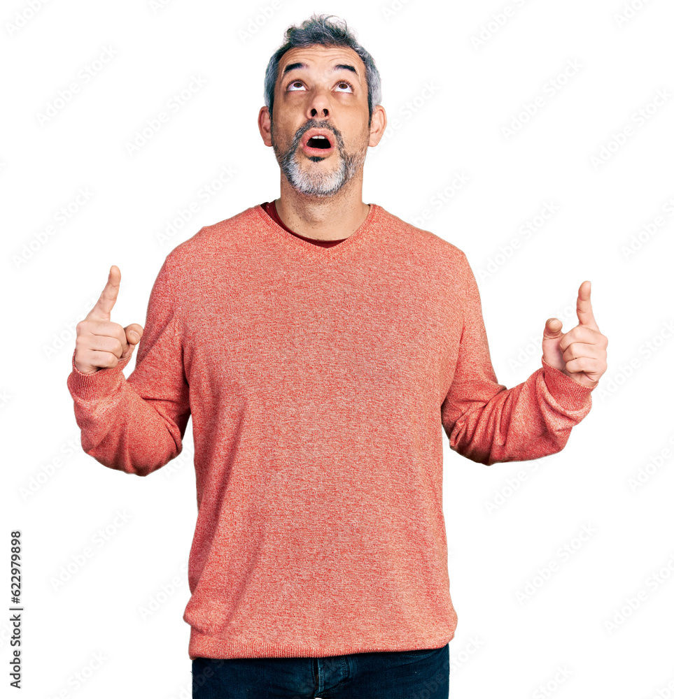 Poster middle age hispanic with grey hair wearing casual sweater amazed and surprised looking up and pointi