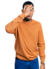 Young african american man wearing casual clothes peeking in shock covering face and eyes with hand, looking through fingers with embarrassed expression.