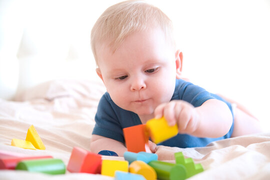 baby boy in blue bodysuit playing with colorful wooden eco toys on bed
