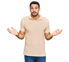 Young hispanic man wearing casual clothes clueless and confused expression with arms and hands raised. doubt concept.