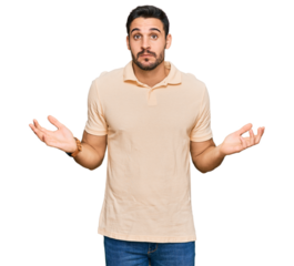 Young hispanic man wearing casual clothes clueless and confused expression with arms and hands raised. doubt concept.
