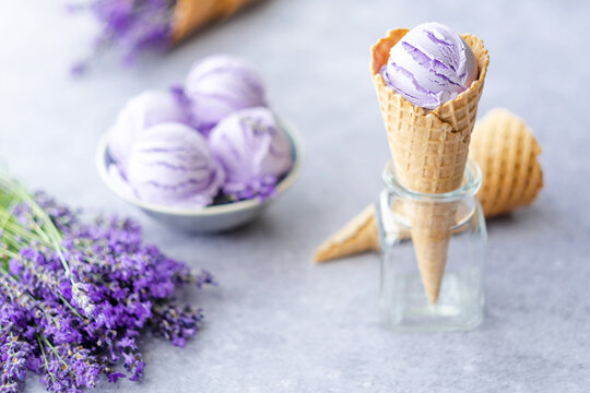 Natural purple ice cream in waffles cone with flowers on gray background. Frozen Dessert. Healthy food 