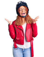 Young latin woman wearing leather jacket holding motorcycle helmet celebrating mad and crazy for...