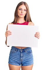 Fototapeta premium Young beautiful blonde woman holding blank empty banner thinking attitude and sober expression looking self confident