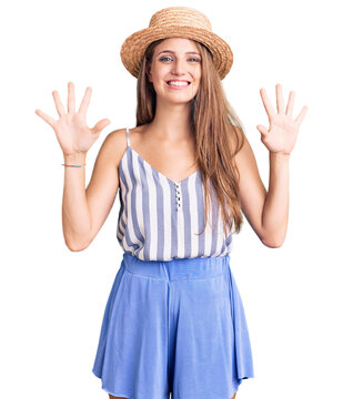 Young beautiful blonde woman wearing summer hat showing and pointing up with fingers number ten while smiling confident and happy.