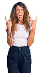 Young hispanic woman with tattoo wearing casual white tshirt shouting with crazy expression doing...