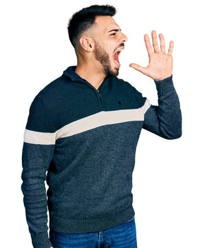 Young hispanic man with beard wearing casual winter sweater shouting and screaming loud to side with hand on mouth. communication concept.